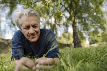 Confident smiling man looking at grass while lying in field - GUSF04436