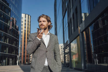 Confident handsome male professional talking on smart phone through speaker at financial district - VPIF02902