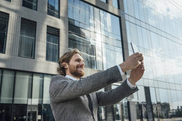 Lächelnde männliche professionelle Aufnahme Selfie gegen Bürogebäude im Stadtzentrum Bezirk - VPIF02908