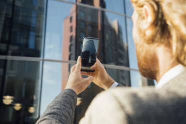 Junger männlicher Unternehmer, der ein Bürogebäude in der Innenstadt mit seinem Mobiltelefon fotografiert - VPIF02909