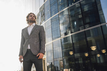 Male professional looking away while standing against office building in downtown district - VPIF02911