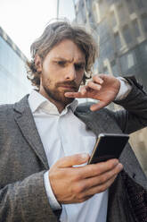 Worried young male entrepreneur using smart phone at financial district in city - VPIF02915