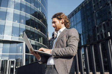 Handsome male professional using laptop in financial district on sunny day - VPIF02920