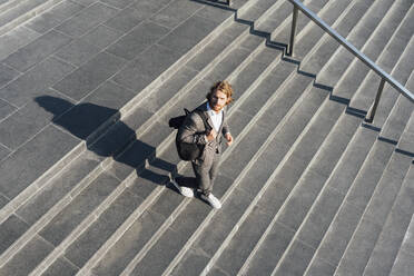 Male professional with bag moving down on staircase in downtown during sunny day - VPIF02926