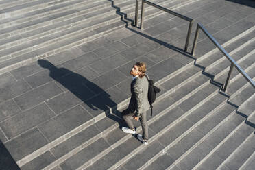 Männlicher Unternehmer mit Tasche, der eine Treppe hinaufgeht, während er in der Innenstadt an einem sonnigen Tag wegschaut - VPIF02927