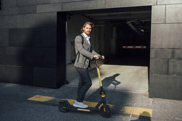 Confident businessman riding electric push scooter to commute in downtown - VPIF02943