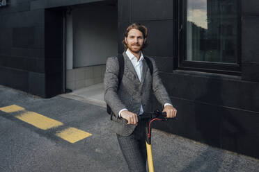Confident handsome male entrepreneur riding electric push scooter to commute in downtown - VPIF02945