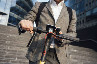 Midsection of male professional using mobile phone while holding electric push scooter handle - VPIF02952