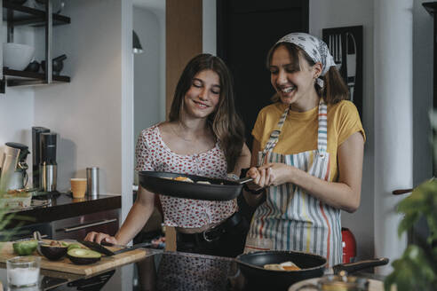 Girlfriends preparing healthy lunch together, frying eggs in kitchen - MFF05989