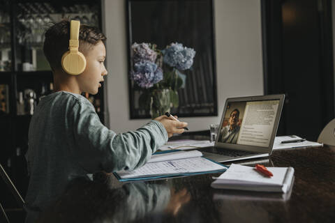 Schoolboy learning at home, using laptop and headphones stock photo