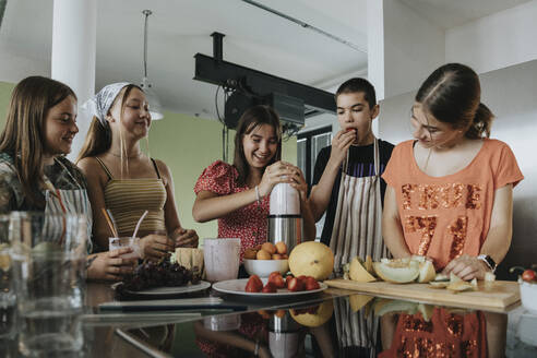 Group of teenagers standing in kitchen, preparing smoothies with a blender - MFF06048