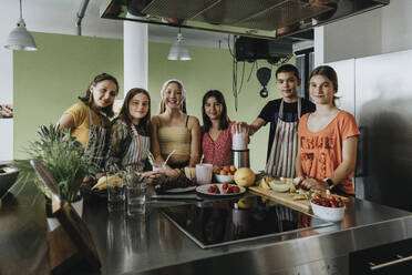 Eine Gruppe Jugendlicher steht in der Küche und bereitet Smoothies mit einem Mixer zu - MFF06049