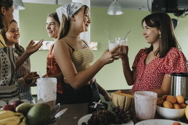 Teenager-Mädchen stehen in der Küche und probieren frische Frucht-Smoothies - MFF06050