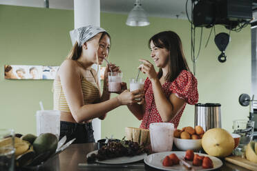 Teenager-Mädchen stehen in der Küche und trinken frische Frucht-Smoothies mit Trinkhalmen - MFF06051