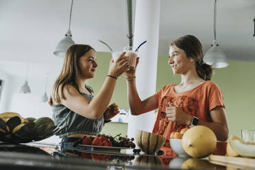 Teenager-Mädchen stehen in der Küche und probieren frische Frucht-Smoothies - MFF06052