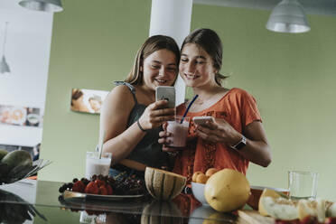 Teenager-Mädchen bereiten frische Fruchtsmoothies zu und teilen Smartphone-Bilder - MFF06054