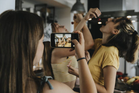 Teenage girl filming friendswith her smartphone, eating cherries stock photo