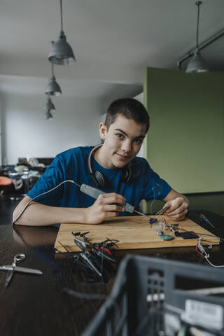 Boy sitting at home using soldering iron stock photo