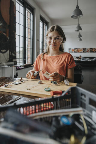 Teenage girl tinkering with soldering iron at home stock photo