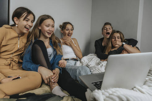 Eine Gruppe von Freundinnen sitzt auf dem Bett und schaut einen Film auf dem Laptop - MFF06078