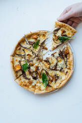 Overhead anonyme Person, die ein Stück schmackhafte Meeresfrüchte-Pizza mit Pilzen und Basilikum gegen weißen Hintergrund - ADSF11764