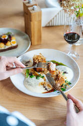 Cropped unerkennbare Person Hände essen Stücke von gebratenem Fleisch mit Trüffeln und frischen Kräutern auf dem Teller im Café serviert - ADSF11782