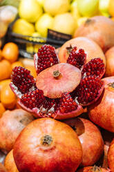 Cute fresh pomegranate placed on heap of fruits on stall in grocery store - ADSF11784