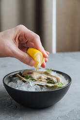Unkenntlich abgeschnittene Person, die Zitrone auf leckere Austern auf einem Eiswürfel auf einer Schale in einem Restaurant drückt - ADSF11788