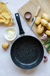 Overhead fresh potatoes and spices placed on cutting board near empty frying pan and napkin on table in kitchen - ADSF11791