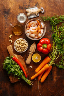 Draufsicht auf verschiedene reife Gemüse und Kräuter neben einer Saftpresse und gekochten Garnelen auf einem Holztisch in der Küche - ADSF11805