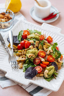 Appetitlicher bunter, gesunder, frischer Salat mit Gemüse und Cashewnüssen, garniert mit Basilikumblättern, serviert auf weißem Teller mit Gabeln - ADSF11815