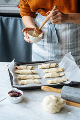 Cook holding bowl and brushing croissants in baking sheet on table - ADSF11823