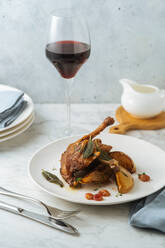 Delicious appetizing roasted quail garnished with pears and leaves served with glass of red wine on light marble table - ADSF11824