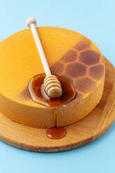 From above delicious honeycomb cake decorated with spoon and fresh liquid honey on blue background - ADSF11847