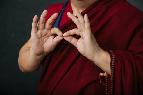 Nahaufnahme der Hände eines betenden tibetischen Mönchs in einem traditionellen roten Gewand mit der symbolischen Geste der Mudra-Hände - ADSF11870