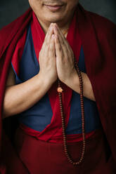 Seitenansicht eines erntebuddhistischen Mönchs in traditioneller roter Kleidung, der Gebetsperlen in der Hand hält - ADSF11871