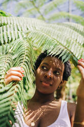 Beautiful woman hiding behind leaves at park - DCRF00636