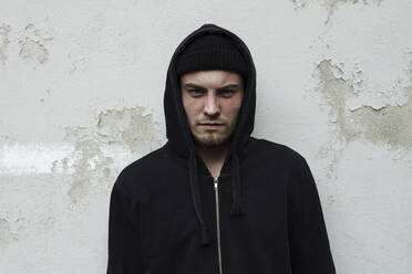 Man wearing hoodie standing against wall - SAJF00039