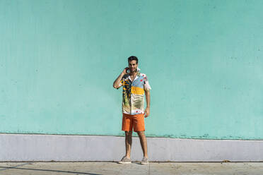 Cool man standing in front of green wall with headphone around his neck - AFVF06986