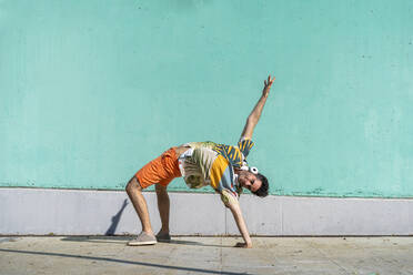 Lässiger Mann, der vor einer grünen Wand Akrobatik betreibt - AFVF06993