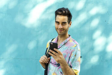 Attraktiver Mann steht vor einer blauen Wand und benutzt ein Smartphone - AFVF07006