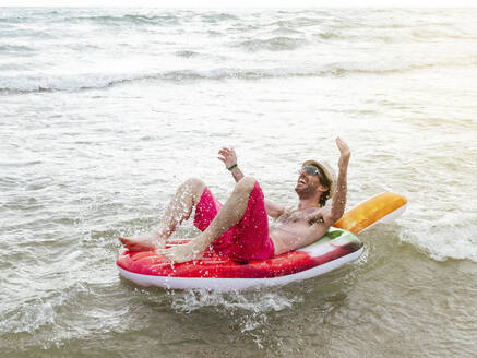 Glücklicher Mann beim Baden im Meer auf einem aufblasbaren Schwimmer - JCMF01177