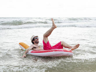 Glücklicher Mann beim Baden im Meer auf einem aufblasbaren Schwimmer - JCMF01178