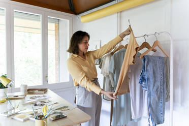 Selbstbewusste junge Modedesignerin, die im Laden stehend ihr Oberteil begutachtet - AFVF07039