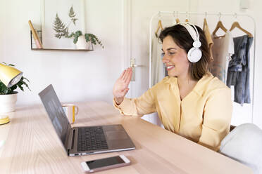 Lächelnde Frau winkt Freunden bei einem Videoanruf über einen Laptop zu Hause zu - AFVF07043