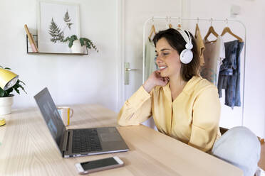 Glückliche junge Frau genießt Videoanruf mit Freunden durch Laptop zu Hause - AFVF07044