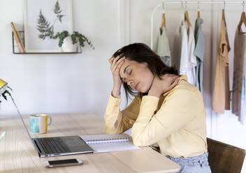 Tired businesswoman with headache and neck pain sitting at table while working from home - AFVF07046