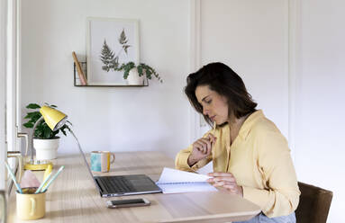 Junge Unternehmerin schaut in ihr Tagebuch, während sie am Laptop sitzt - AFVF07047