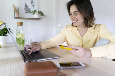 Lächelnde schöne junge Frau genießt Online-Shopping durch Laptop zu Hause - AFVF07055