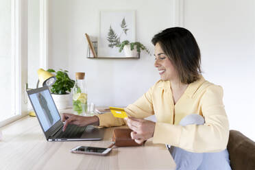 Glückliche schöne junge Frau, die einen Laptop zum Online-Shopping zu Hause benutzt - AFVF07056